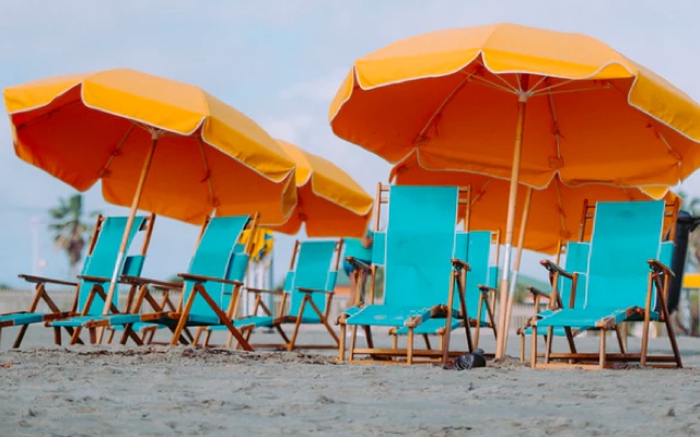 A photo on the beach featuring turquiose beach chairs and orange umbrellas.