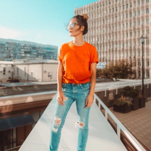 A photo of Sophie in an orange shirt and ripped jeans, standing on top of a building.