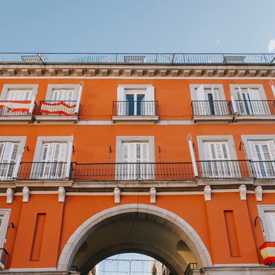 Photo of an orange stucco building with white shuttered windows and an archway below.