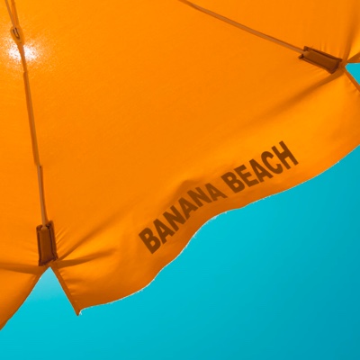 Photo looking towards the sky showing the underside of an orange umbrella with the words Banana Beach.